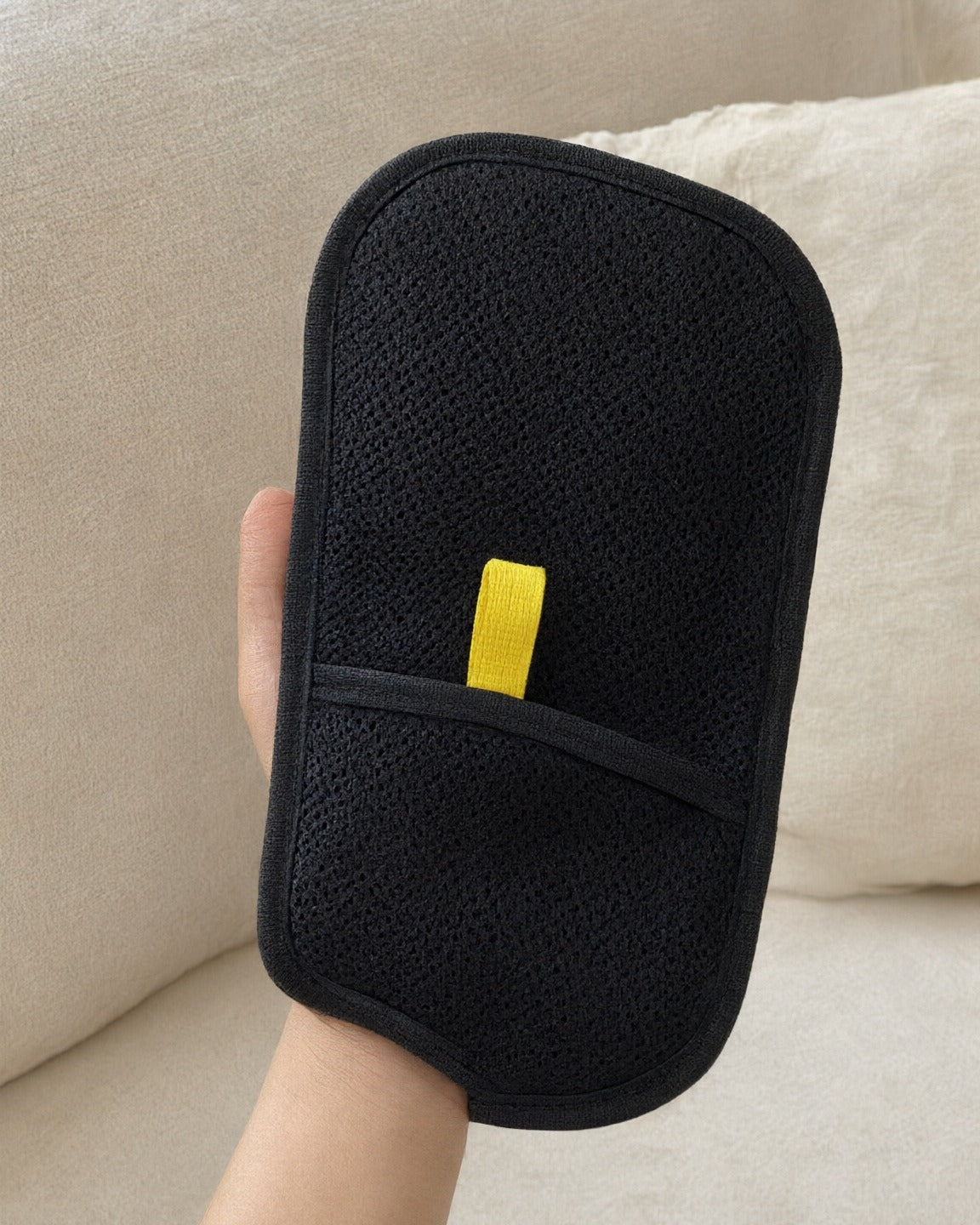 Hand holding the FurSwipe glove: black mesh pocket and yellow pull tab